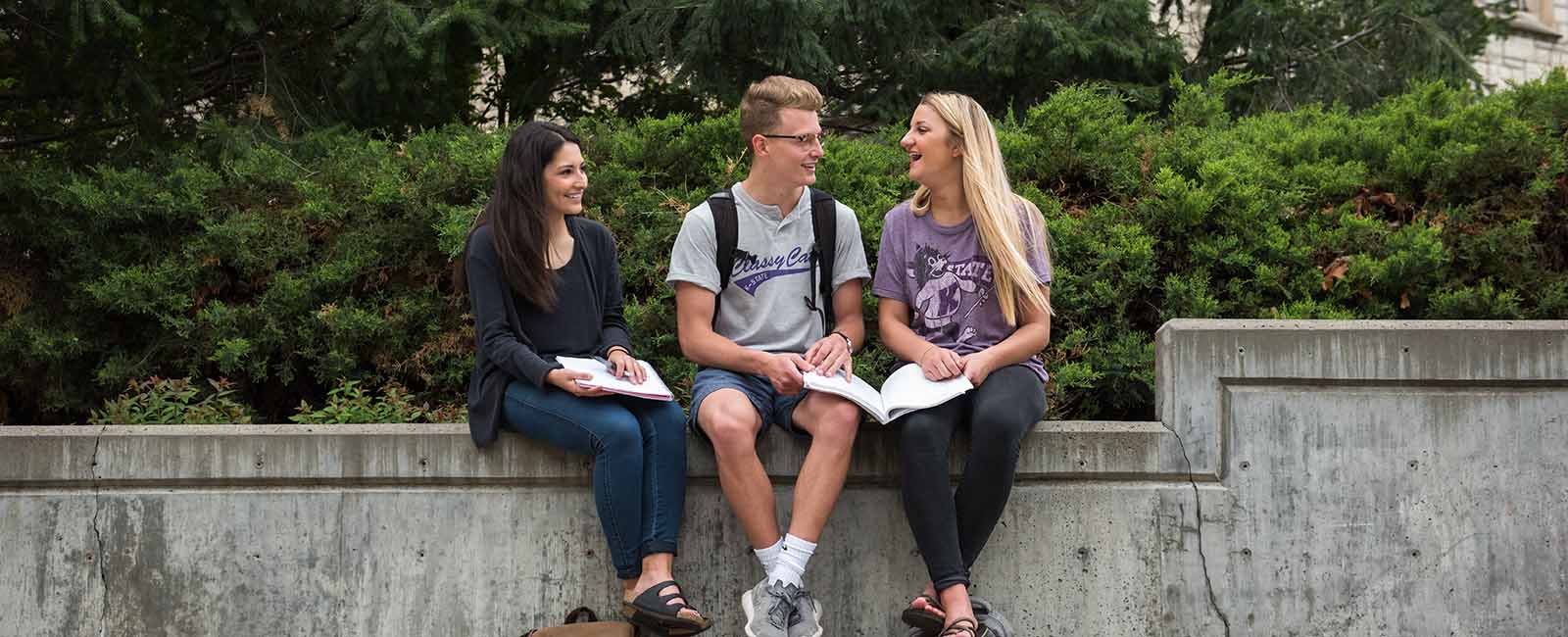 Students sitting on wall outside on K-State campus