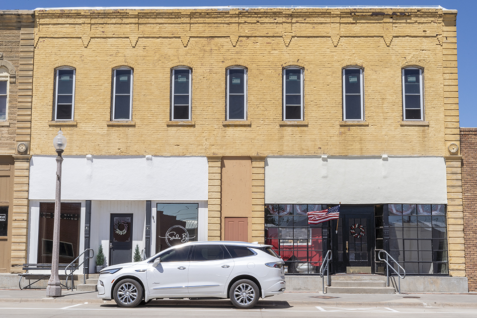 A white SUV is parked in front of a yellow-brick building in downtown Jetmore, Kansas.