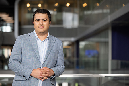 Davood Pourkargar wears a gray suit jacket and poses for a portrait in a large academic hall.