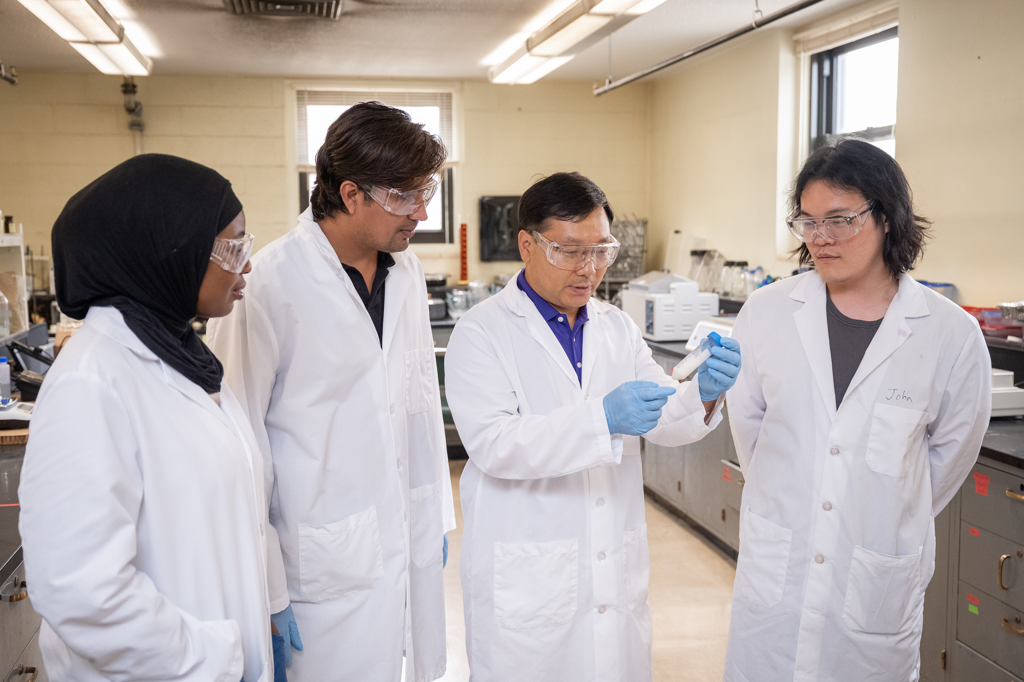 Yonghui Li, in a white labcoat, holds up a test among a group of other researchers.