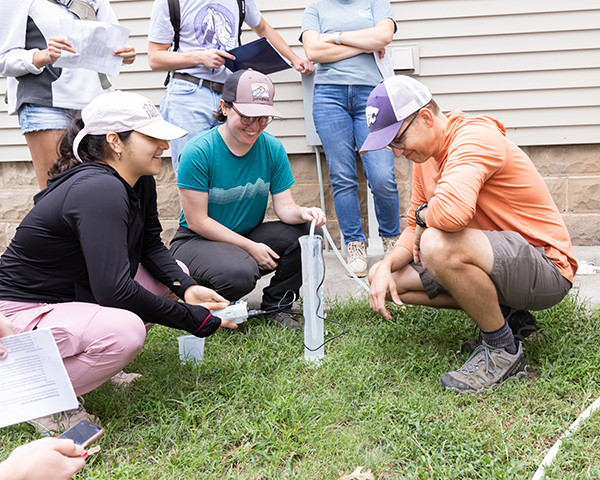 A researcher and students gather around a tube in the ground to test the water.