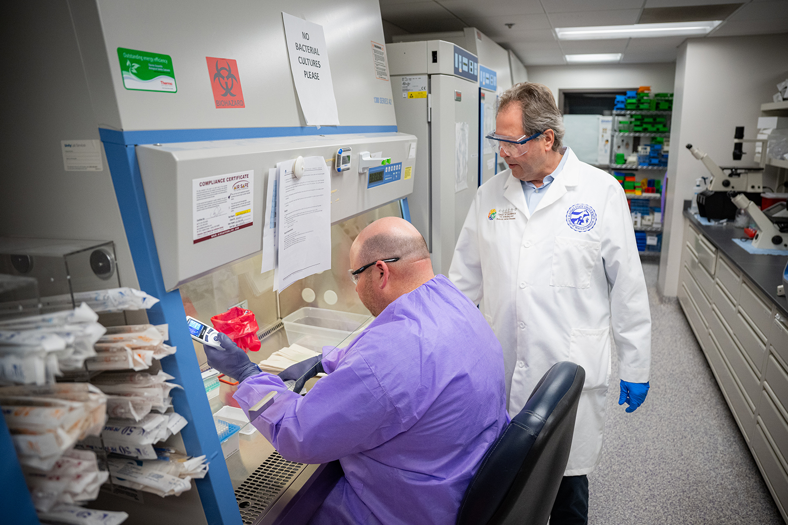 A postdoctoral resercher works under a hood in a lab as a principal investigator resercher supervises.