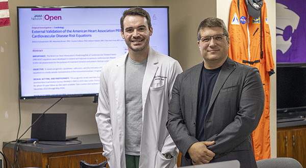 A doctoral student in a labcoat and a professor in a gray sport coat pose for a portrait.