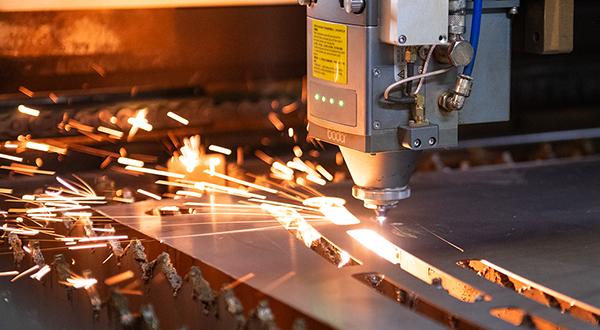 A laser etcher moves across a metal sheet, the tip of the laser creating several sparks.