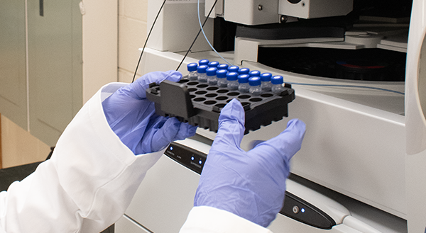 gloved hands load vials into a piece of lab equipment